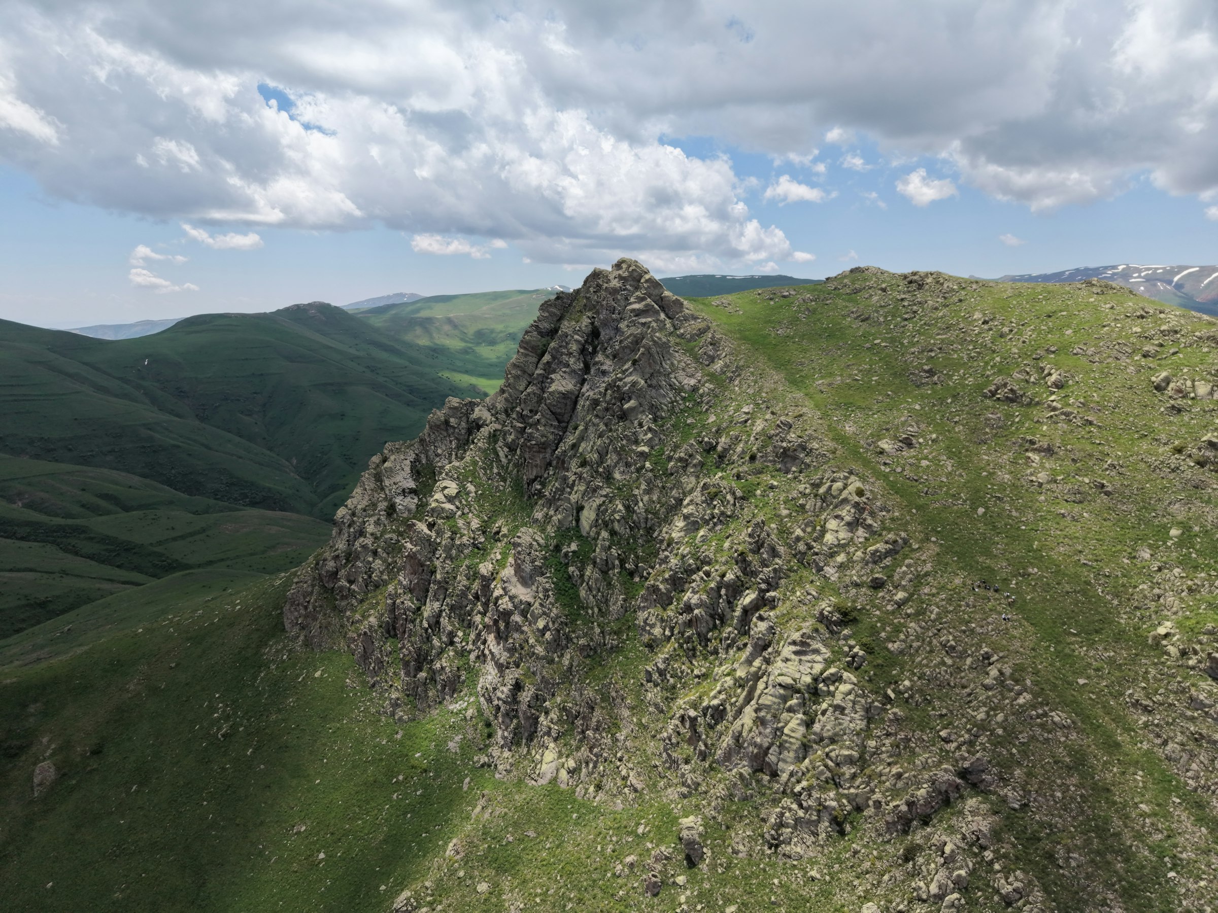 Aerial view of a rocky peak above green slopes